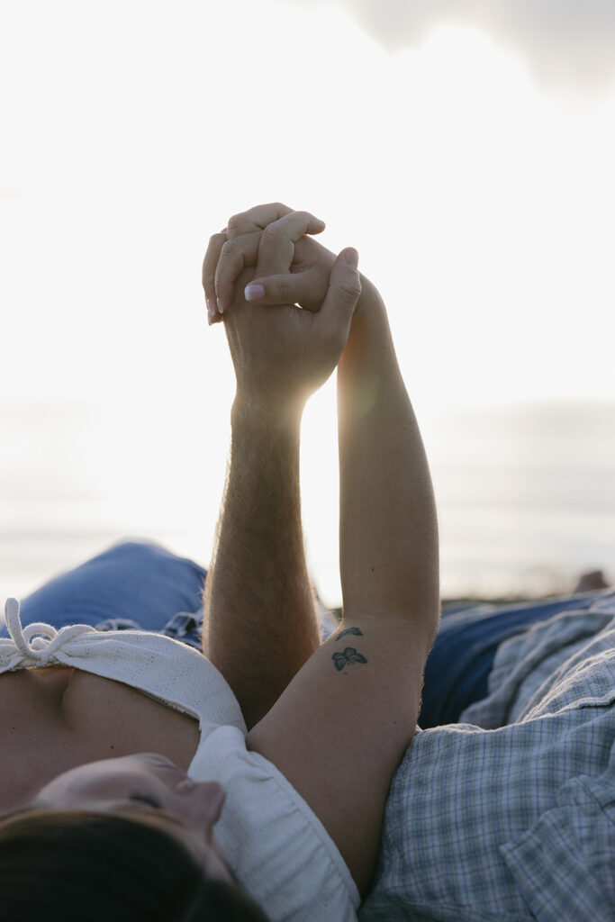 A couple interlocks their fingers as the California sun shines between them during their engagement pictures san diego
