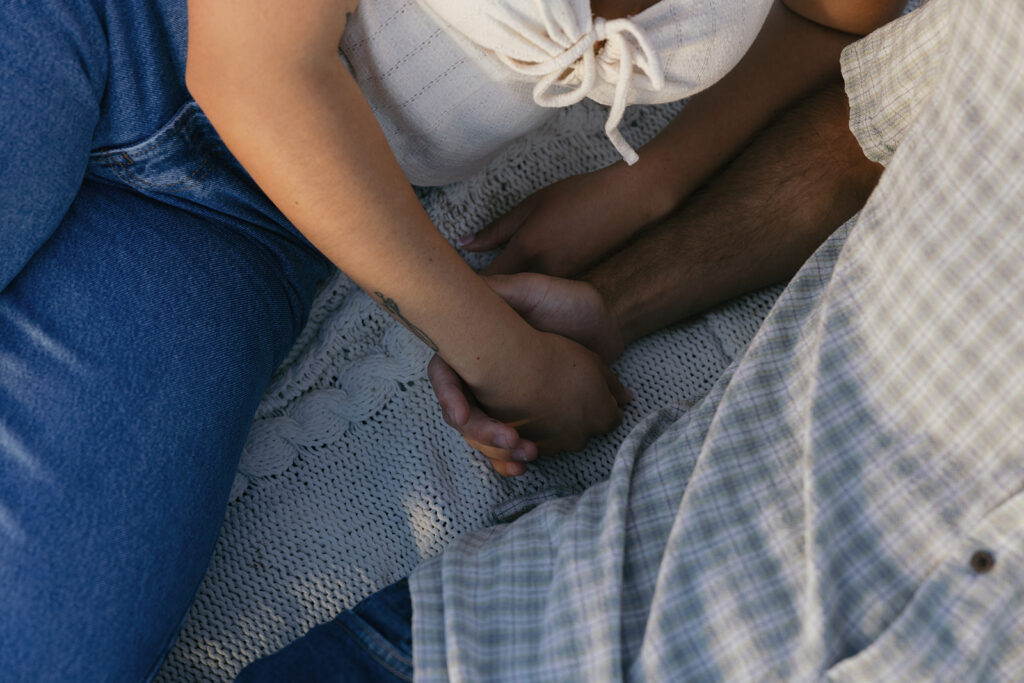 A close up shot of a couple holding hands atop a knit blanket during their engagement photos southern california 