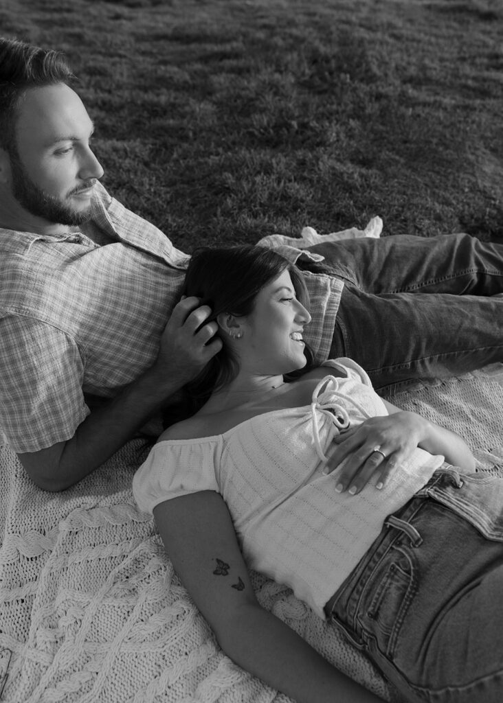 A b+w image of a couple relaxing on a blanket in the grass during a photoshoot to celebrate their san diego engagement 