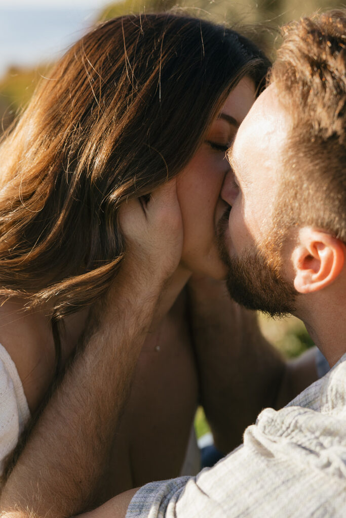 A couple share a kiss in the golden light of a west coast sunset during a pacific beach engagement photoshoot